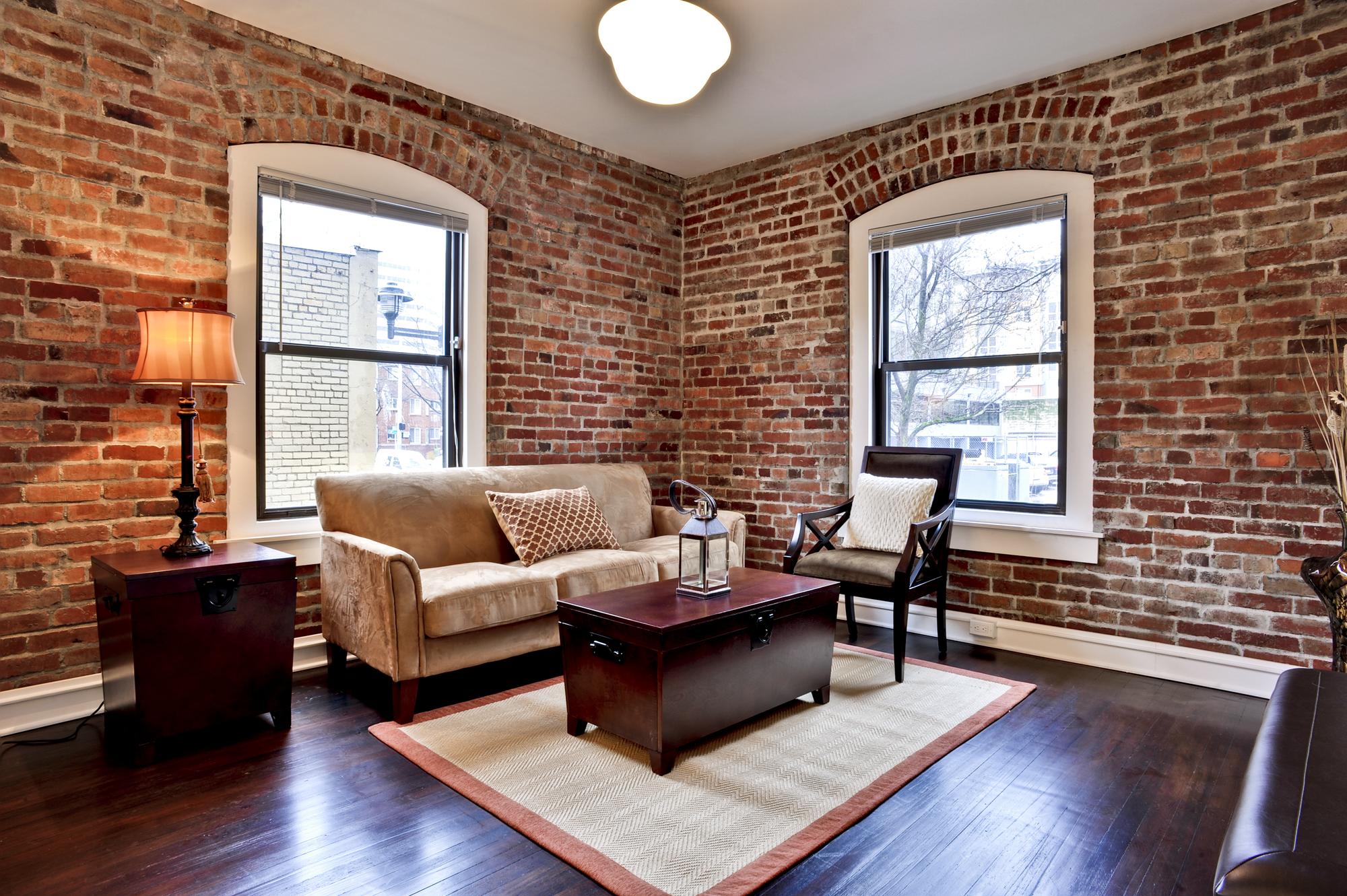 Renovated living room with exposed brick walls and arched windows at Adams Apartments